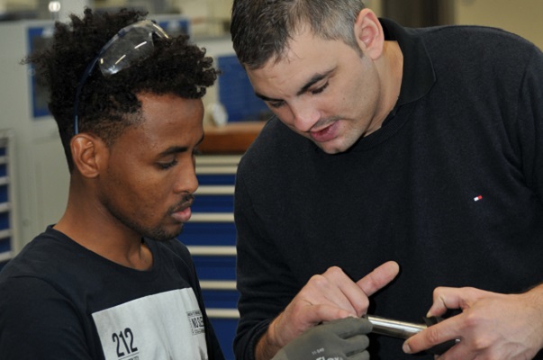 Ausbilder Christoph Hogen demonstriert Abdirazaq Aden Ahmed die Bearbeitung eines Metallstücks (Foto: Renolit).